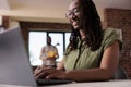 Smiling freelancer relaxing looking at funny content on laptop while roommate is reading a book