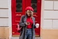 Smiling french woman in glasses texting message standing near coffee house. Outdoor portrait of cheerful girl in beret