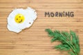 Smiling fried egg lying on a white plate on a wooden cutting board with bunch of dill and morning inscription near it. Royalty Free Stock Photo