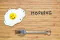 Smiling fried egg lying on a wooden cutting board with morning inscription near it. Classic Breakfast concept.