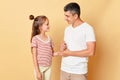 Smiling friendly man and little kid girl standing together isolated over beige background talking having pleasant upbringing Royalty Free Stock Photo