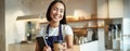 Smiling friendly waitress in coffee shop, barista giving out takeaway order, cappuccino in paper cup for takeout