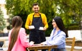 Smiling friendly waitress serving coffee drinks to diverse male friends meeting at cafe table, cafeteria server and Royalty Free Stock Photo