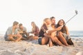 Smiling friends sitting on sand singing and taking selfies Royalty Free Stock Photo