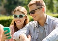 Smiling friends with smartphone sitting in park