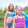 Portrait of smiling friends in swimwear standing with pool raft and squirt gun at lakeshore