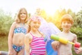 Portrait of smiling friends in swimwear standing with pool raft and squirt gun at lakeshore