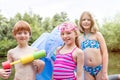 Portrait of smiling friends in swimwear standing with pool raft and squirt gun at lakeshore