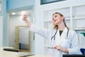 Smiling fun beautiful young doctor woman with stethoscope at hospital reception. Female doctor in medical gown doing