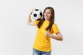 Smiling fun European young woman, football fan in yellow uniform holding soccer ball showing thumbs up gesture isolated