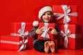Smiling funny child boy in Santa red hat fell asleep with Christmas gifts in hand in hand on red background. Royalty Free Stock Photo