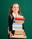 Smiling funny little schoolkid girl with backpack hold books on green blackboard. Childhood lifestyle concept. Education