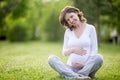 Smiling future mom sitting cross-legged on grass lawn