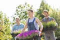 Smiling gardeners carrying crates with flower pots at plant nursery