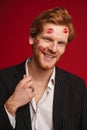 Man with lipstick marks on face posing isolated over red wall