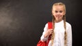 Smiling girl with backpack standing against blackboard, ready to start school