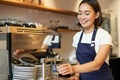 Smiling girl barista in cafe, preparing cappuccino in coffee machine, steaming milk, wearing uniform apron Royalty Free Stock Photo