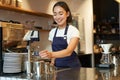 Smiling girl barista in cafe, preparing cappuccino in coffee machine, steaming milk, wearing uniform apron Royalty Free Stock Photo