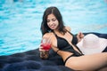 Smiling girl in black bikini holding a cocktail sitting on mattress in swimming pool on a blurred background of resort Royalty Free Stock Photo