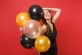 Smiling girl in black dress celebrate putting hand on head hold air balloons isolated on red background. St. Valentine`s Royalty Free Stock Photo