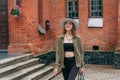 A smiling girl with blond long hair, in black leggings, a tank top, a beige jacket and a hat Royalty Free Stock Photo