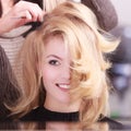Smiling girl with blond wavy hair by hairdresser in beauty salon Royalty Free Stock Photo