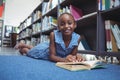 Smiling girl with book lying by shelf in library Royalty Free Stock Photo