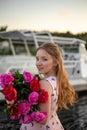 Vertical portrait of a young blonde with a bouquet of bright peonies on a yacht background