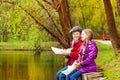 Smiling girl and boy sit near nice pond playing Royalty Free Stock Photo