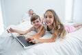 Smiling girl and boy using laptop on bed in bedroom at home Royalty Free Stock Photo