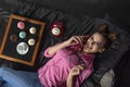 Smiling girl with bright makeup and bun hairstyle lies on black bed and talks on retro phone. Cupcakes with cream and white cup on