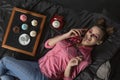 Smiling girl with bright makeup lies on black bed and talks on retro phone. Cupcakes with multicolored cream