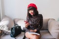 Smiling girl with brown hair in trendy french beret and vintage short dress writing message to friend. Portrait of