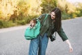 A smiling girl with a camera around her neck holds a green backpack on her shoulder, from which a cute dog looks out Royalty Free Stock Photo