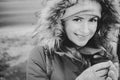 Smiling girl with coffee in warm jacket with fur hood, black and white. Pretty woman in hooded jacket in the city. Urban lifestyle Royalty Free Stock Photo