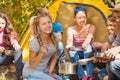 Smiling girl cooks soup in pot near yellow tent