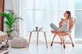 Time to relax. Smiling girl drinking hot tea, sitting in wicker chair and looking out of window at home Royalty Free Stock Photo