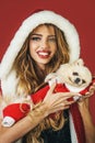 Smiling girl in fur hat hugging small dog. Christmas woman and puppy in Santa costume. Sexy beautiful female with Royalty Free Stock Photo