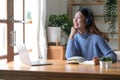 Smiling girl in headphones sitting at a desk looking outside and using a laptop to study online. Smart young women who Royalty Free Stock Photo