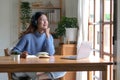 Smiling girl in headphones sitting at a desk looking outside and using a laptop to study online. Smart young women who are happy Royalty Free Stock Photo