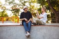 Smiling girl with headphones taking photo of young guy with skateboard on cellphone spending time together at modern Royalty Free Stock Photo