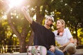 Smiling girl with headphones and young guy with skateboard happily taking photos on frontal camera of cellphone together Royalty Free Stock Photo