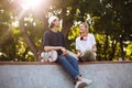 Smiling girl with headphones and young guy with skateboard joyfully spending time together at modern skatepark Royalty Free Stock Photo