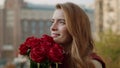 Smiling girl holding bunch outdoors. Cheerful woman smelling flowers on street. Royalty Free Stock Photo