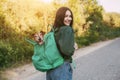 A smiling girl is holding a green backpack on her shoulder, from which a cute dog looks out. A girl and her friend travel together Royalty Free Stock Photo