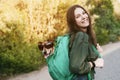 A smiling girl is holding a green backpack on her shoulder, from which a dog in sunglasses looks out. A girl and her friend travel Royalty Free Stock Photo