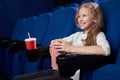 Smiling girl holding popcorn bucket, sitting in cinema.