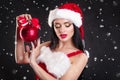 Smiling girl holding a red Christmas tree balls. Women on dress and santa`s hat. Santa`s helper .Attractive happy girl in santa h Royalty Free Stock Photo