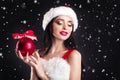 Smiling girl holding a red Christmas tree balls. Women on dress and santa`s hat. Santa`s helper .Attractive happy girl in santa h Royalty Free Stock Photo