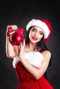 Smiling girl holding a red Christmas tree balls. Women on dress and santa`s hat. Santa`s helper .Attractive happy girl in santa h Royalty Free Stock Photo